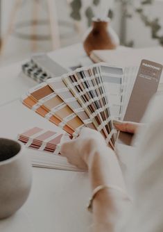 a woman is holding some paint samples in her hand while she sits at a table