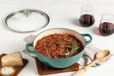 a pot of food sitting on top of a wooden cutting board next to two glasses of wine