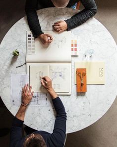 two people sitting at a table working on architectural drawings