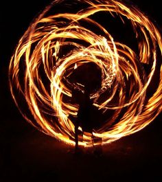 a person standing in the dark with fire spinning around their body and arms, all lit up