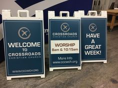 three signs are on the floor in front of a blue and white sign that says welcome to worship