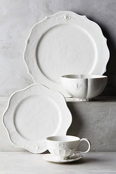 white porcelain dishes and cups are stacked on top of each other in front of a gray wall