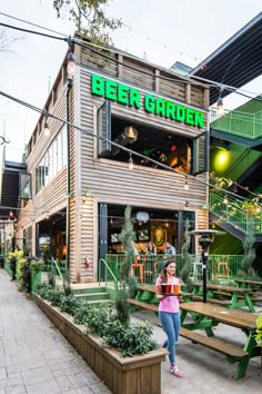 a woman standing in front of a beer garden building with green lettering on the side