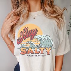 Embrace beachy vibes and Christian inspiration with our "Stay Salty" Comfort Colors shirt. Crafted from 100% ring-spun cotton, this garment-dyed tee offers unmatched comfort and coziness. The captivating design features a stunning wave and sunset, reminding you to "Stay Salty"  as stated in Matthew 5:13 states: "You are the salt of the earth. But if the salt loses its saltiness, how can it be made salty again? It is no longer good for anything, except to be thrown out and trampled underfoot." Th Beachy Relaxed Fit Shirt With Letter Print, Cotton Letter Print Shirt For Beach Party, Casual Letter Print Shirt For Beach Party, Casual Shirt With Letter Print For Beach Party, Beachy Cotton Shirt With Relaxed Fit, Beachy Graphic Print Shirt For Beach Party, Beachy Relaxed Fit Cotton Shirt, Beachy Crew Neck Shirt With Letter Print, Trendy Pre-shrunk Beach Shirt