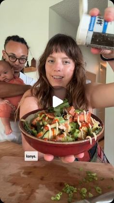 a woman holding a bowl of salad with two men in the background