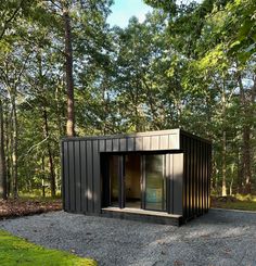 a small black building sitting in the middle of a forest