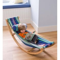 a little boy sitting in a hammock reading a book