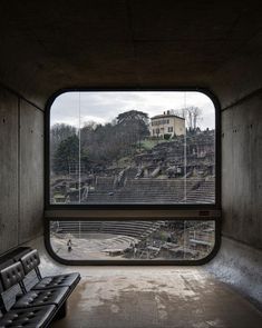 an empty room with a bench in front of the window looking out at a roman amphit