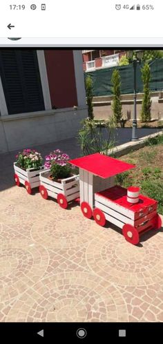 a red and white train cart with flowers in it on the ground next to a building