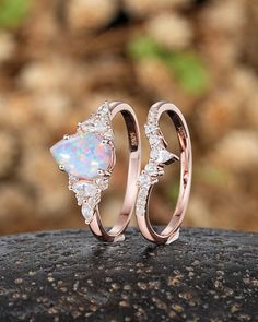 two wedding rings with opal and diamond accents on top of a rock in front of some rocks