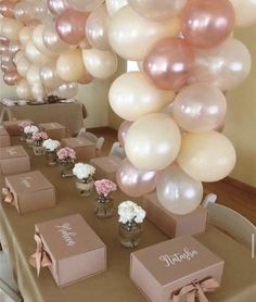 a table topped with lots of pink and white balloons next to boxes filled with flowers