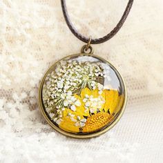 a necklace with flowers on it sitting on a white cloth covered surface, next to a flower pot