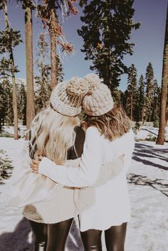 two women hugging each other while standing in the snow with trees and snow covered ground behind them