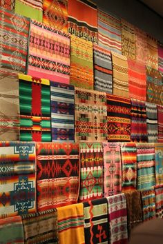 a wall covered in lots of different colored fabrics and rugs with designs on them