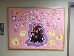 a group of people standing in front of a pink bulletin board with words on it