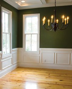 an empty room with green walls and white trim around the windows, chandelier and wood flooring