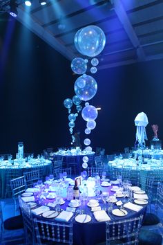 To access the dining area guests made their way through an opulent deep wall of fabric columns, emulating waves and shafts of light in the sea. Dining tables were dressed in four different shades of blue cloths, surrounded with clear perspex chairs. Bubble, coral and internally illuminated jelly fish table centres combined with creative under the sea lighting brought the space to life and left guests utterly in awe as 3mtr jellyfish acrobats danced the night away over the top of the tables. Water Themed Decorations, Underwater Theme Sweet 16, Under The Sea Luxury Party, Under The Sea Gala Dress, Dinner And Dance Theme Ideas, Under The Sea Debut Theme, Under The Sea Party Theme Decoration, Jellyfish Quince Theme, Prom 2023 Theme