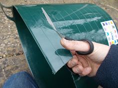 a person holding scissors in their left hand near a green box with stickers on it