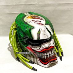 a green and white mask with yellow wires attached to it's face, on a white surface