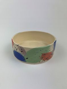 a white bowl with multicolored paint splattered on the inside and outside