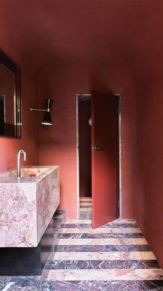 a bathroom with red walls and marble counter tops, along with a striped tile floor