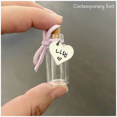 someone is holding a tiny bottle with a heart shaped tag attached to it that says july