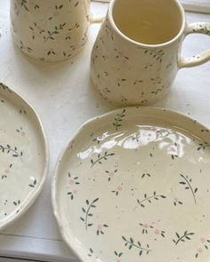 two white plates with flowers on them next to a mug