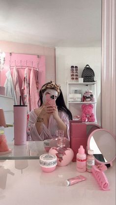 a woman taking a selfie in front of a mirror with pink accessories around her