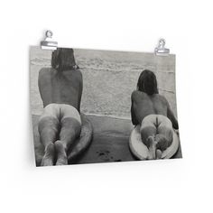 two women sitting on surfboards in front of the ocean, with their backs turned to the camera