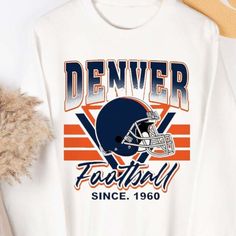 a white denver football t - shirt with an orange and blue graphic on the front