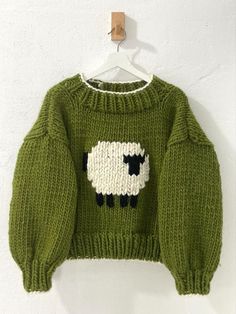 a green sweater with sheep on it hanging from a hanger against a white wall