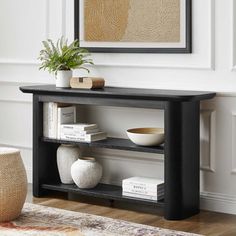 a black shelf with books and vases on it in front of a white wall