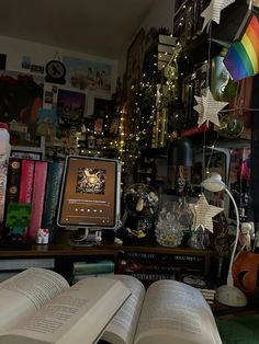 an open book sitting on top of a desk next to a computer monitor and bookshelf