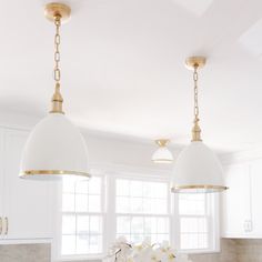 two lights hanging over a kitchen island with flowers on the counter and white cabinets in the background