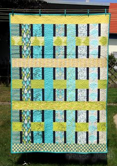 a blue and green quilt hanging from a clothes line in the grass near a house