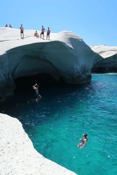 some people are swimming in the water near a cave