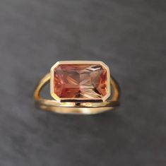 This stunning 14k yellow gold and sunstone statement ring features a solitaire emerald cut color changing sunstone in a bezel setting. This beautiful sunstone features shades of orange, red, yellow and green depending on how the light hits it! The ring itself features a split shoulder style giving more room for light to shine through this beautiful stone. This beautiful high polish cocktail ring makes for a great statement! Stone Significance:  Known as the stone of joy, sunstone is said to inspire good nature + an enjoyment of life. It is highly effective in cleansing auras and chakras. ⊹ 14k Yellow Gold + Sunstone ⊹ Stamp reads 14k ⊹ Excellent Condition ⊹ Ring Size: 7 ⊹ Sunstone: 12.1mm x 8mm, Approx 3.98 TCW Sunset Ring, Orange Sapphire Ring, Orange Sapphire, Yellow And Green, Shades Of Orange, Green Tourmaline, Bracelets And Charms, Gift Accessories, Cocktail Ring