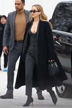 a man and woman walking next to each other in front of a black car on the street