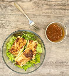 a glass bowl filled with salad next to a fork and spoon on top of a wooden table