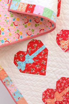 a close up of a quilt on a bed with flowers and heart shaped blocks in the center