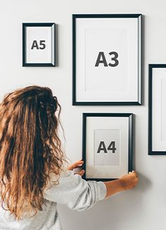 a woman is placing four frames on the wall