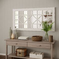 a wooden table topped with a vase filled with green plants next to a wall mounted mirror