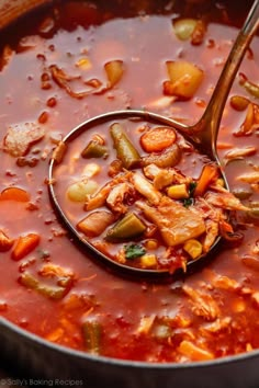 a ladle full of soup with meat and vegetables being stirred by a wooden spoon