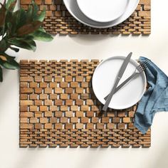 two placemats with white plates and silverware on them next to a potted plant