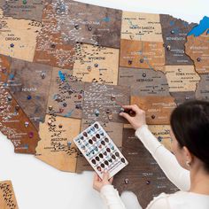 a woman pointing at a map on the wall with stickers and magnets attached to it