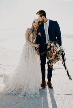 a bride and groom standing in the snow with their arms around each other holding bouquets