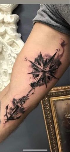 a black and white photo of a compass tattoo on the left arm with watercolors