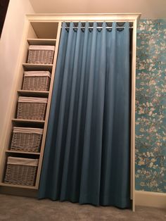 a closet with blue curtains and baskets on the bottom shelf, next to a wallpapered wall