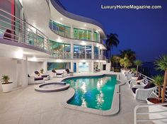 a large house with a swimming pool in the middle of it at night, overlooking the ocean