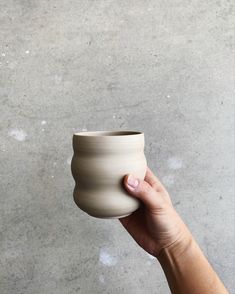 a hand holding a small white vase in front of a gray concrete wall and floor